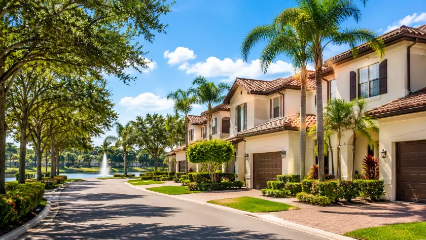 Rua arborizada com townhomes na Flórida, paisagismo tropical e lago com fonte ao fundo